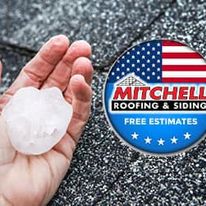 Hand holding a golf ball sized hail stone over roofing shingles.